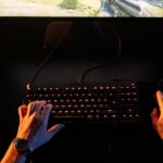 A gamer intensely playing a first-person shooter game on a computer setup indoors at night.