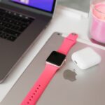 A neatly arranged desk with a laptop, iPad, smartwatch, AirPods, and candle.