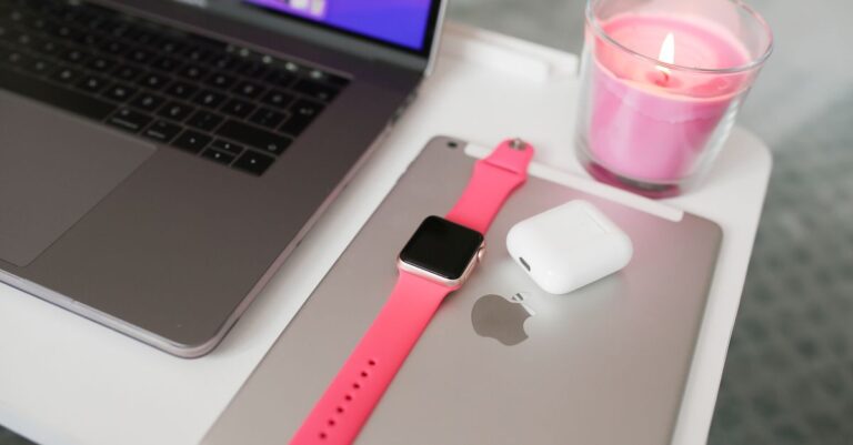 A neatly arranged desk with a laptop, iPad, smartwatch, AirPods, and candle.