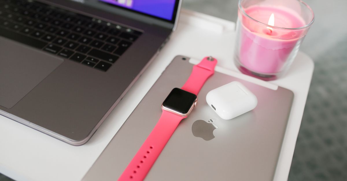 A neatly arranged desk with a laptop, iPad, smartwatch, AirPods, and candle.