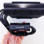 Close-up of a CPU cooler with a 'be quiet!' logo held in hand against a white background.