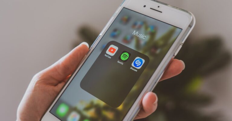 Hand holding a smartphone displaying popular music apps like Spotify and Shazam in a close-up shot.