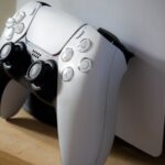 Close-up of PlayStation 5 with DualSense controller on a wooden shelf.