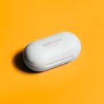 White Samsung wireless earbuds case on a bright yellow background, showcasing sleek tech design.