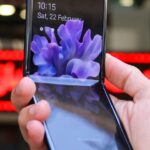 Close-up of a modern flip smartphone held in hand, showcasing innovative technology outdoors in a bustling city.