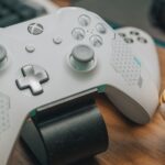 Close-up of an Xbox game controller with a toy, mouse, and keyboard on a desk, showcasing a gaming setup.