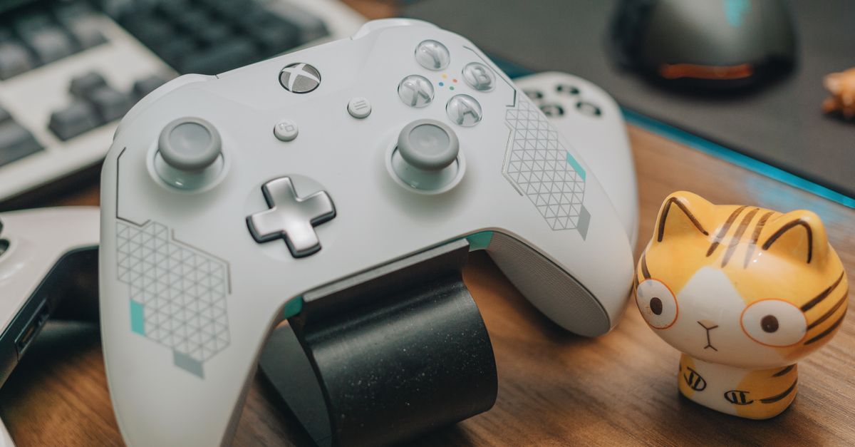 Close-up of an Xbox game controller with a toy, mouse, and keyboard on a desk, showcasing a gaming setup.