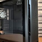 A modern black computer case with tempered glass panel on a wooden desk, ideal for tech enthusiasts.
